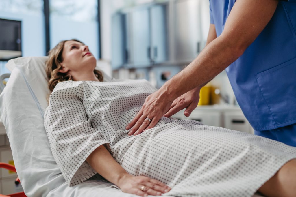 ER doctor palpating woman's abdomen, using hands and steady pressure.